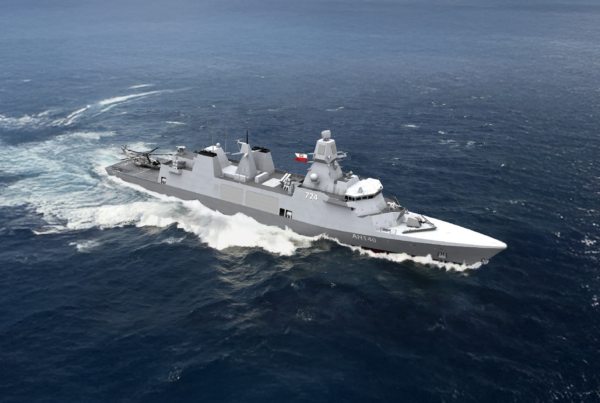 Gray military warship sailing through blue ocean under a clear sky, viewed from above with wake at the stern.
