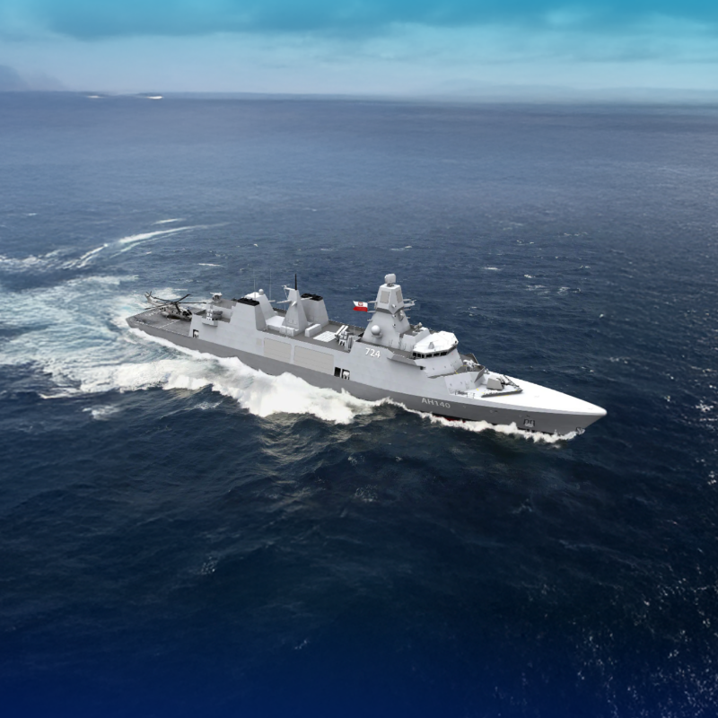 Gray military warship sailing through blue ocean under a clear sky, viewed from above with wake at the stern.